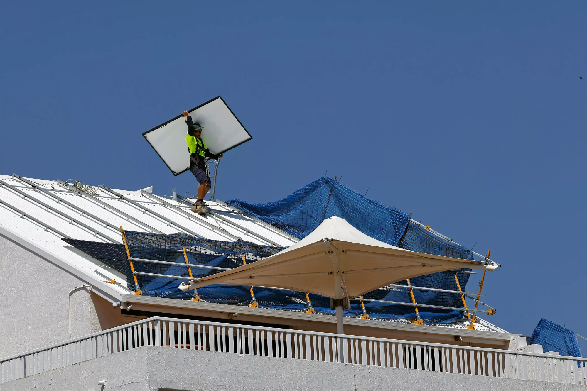 Worker securing a tarp on a damaged roof during rainy weather focusing on safety harness usage